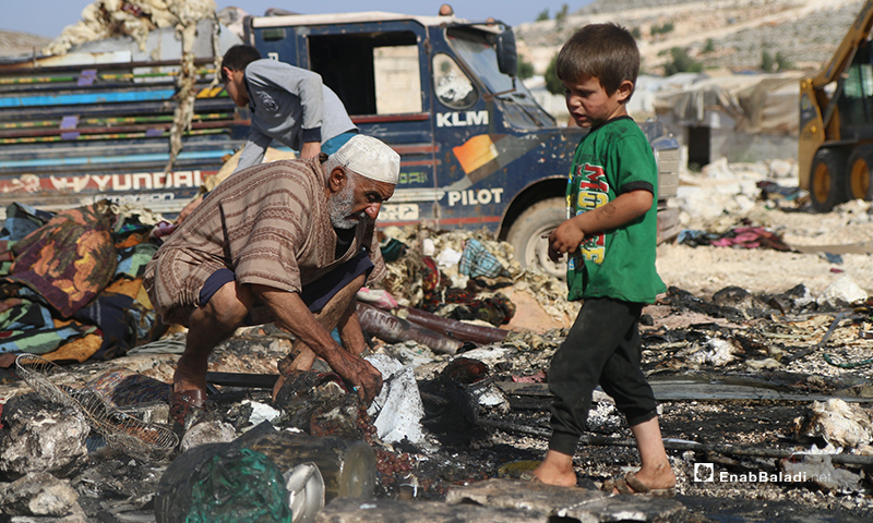 طفل صغير ورجل مسن يبحثون عما لم يحرق من خيمتهم في مخيم دير حسان التابع للدانا في ريف إدلب الشمالي- 17 من أيار (يوسف غريبي/عنب بلدي).