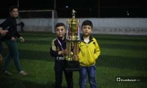 طفلان يحملان كأس بطولة دوري نجوم الشمال بعد انتهاء المباراة النهائية بفوز فريق عقربات على فريق دير حسان في إدلب - 3 أيار 2020 (عنب بلدي)