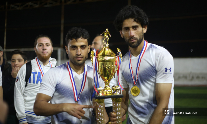 لاعبان يحملان كأس بطولة دوري نجوم الشمال الرابع بعد انتهاء المباراة النهائية بين فريقي عقربات ودير حسان على ملعب قاح في إدلب - 3 أيار 2020 (عنب بلدي)