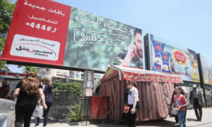 مواطنون يسيرون تحت لوحة إعلانية لأكبر مشغل للهاتف المحمول في سوريا سيريتل المملوك من رامي مخلوف- 11 من أيار 2020 (AFP)