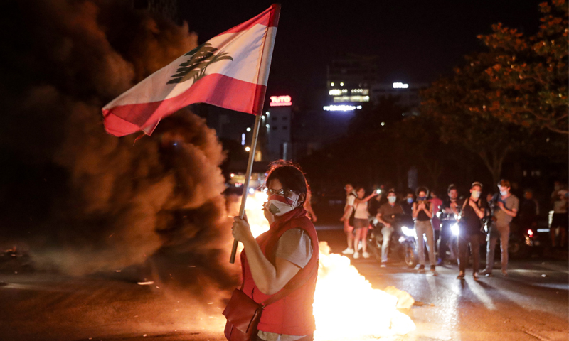 متظاهرة ترفع علم لبنان خلال قطع أحد الطرق بالإطارات المشتعلة احتجاجًا على انخفاض سعر صرف الليرة - 11 حزيران 2020 (فرانس برس)