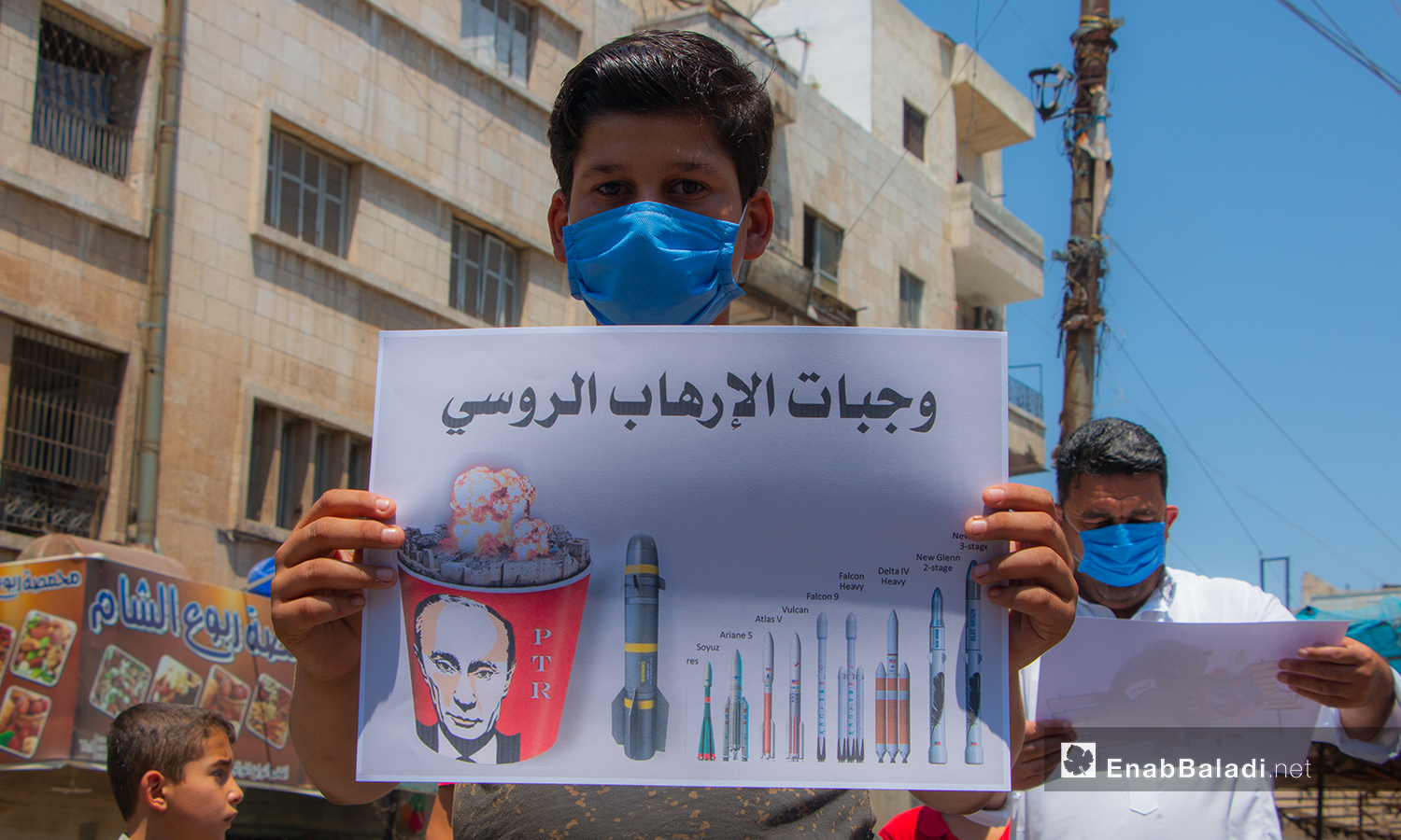 طفل يحمل لافتة تحوي أنواع الصواريخ التي استهدفت الشعب السوري - 10 تموز 2020 (عنب بلدي/أنس الخولي)