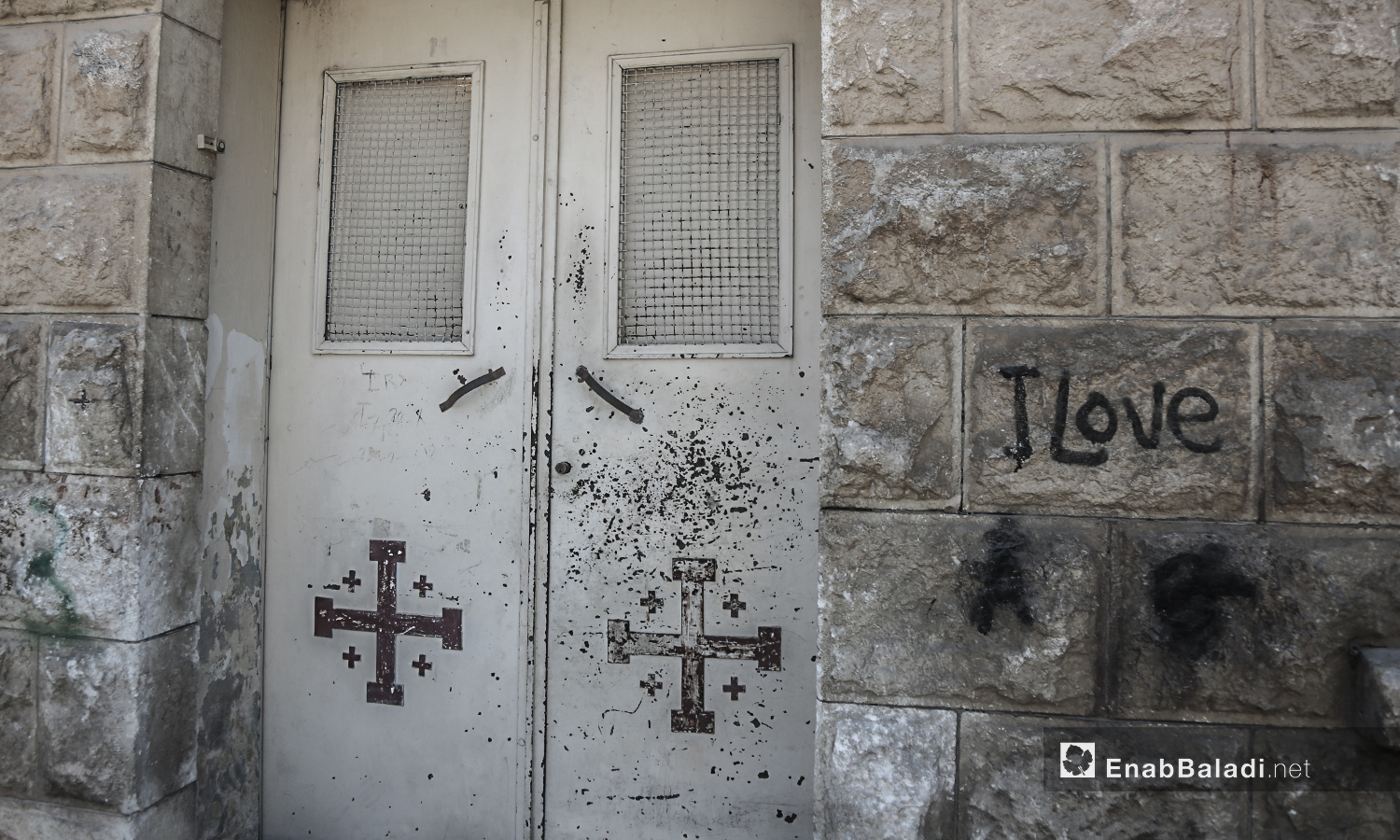 باب حديدي لكنيسة "مار يوسف" تظهر عليه علامات الصدأ فوق الصلبان المرسومة على واجهته - تموز 2020 (عنب بلدي)