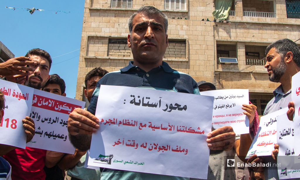 رجل يحمل لافتة لضامني محور أستانة في مظاهرة بمدينة إدلب - 3من تموز 2020 (عنب بلدي/أنس الخولي)