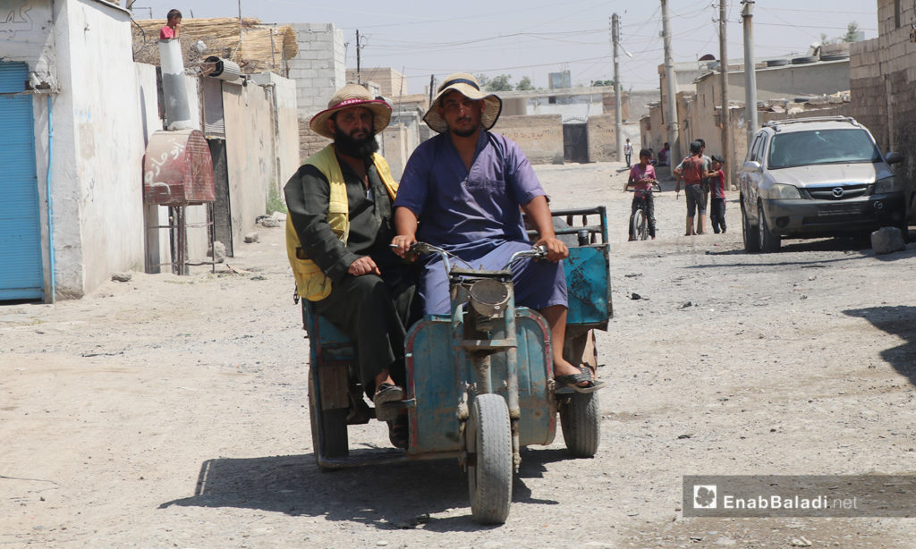 شخصان يركبان شاحنة بثلاث عجلات في مدينة الرقة - 11 تموز 2020 (عنب بلدي/عبد العزيز صالح)