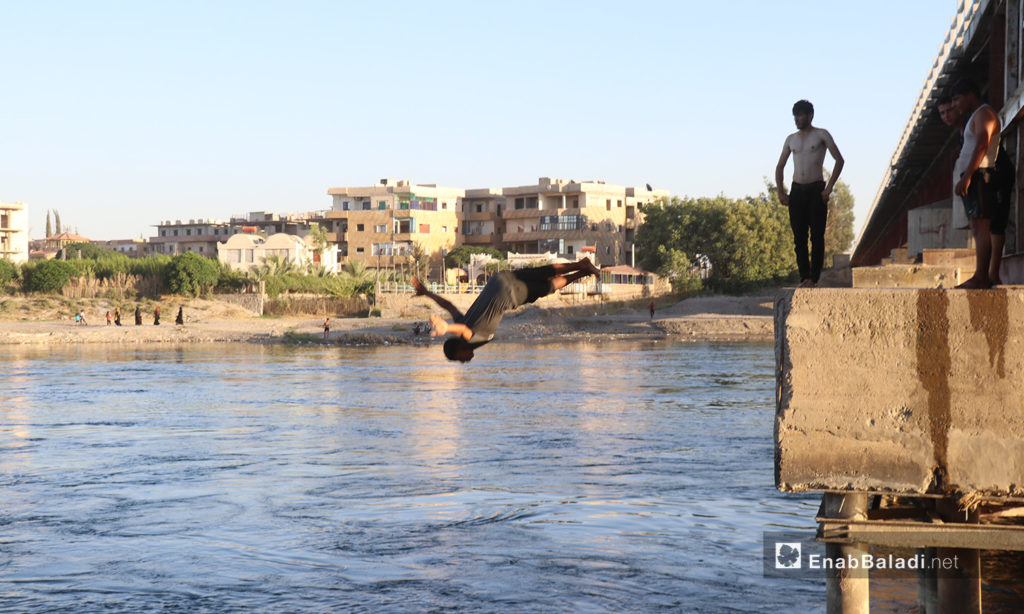 شاب يقفز للسباحة من جسر يمر فوق نهر الفرات في محافظة الرقة - 24 تموز 2020 (عنب بلدي/عبد العزيز صالح)