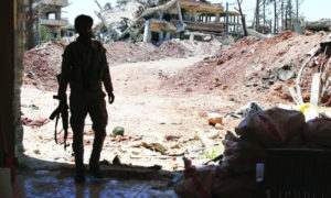 مقاتل يحمل السلاح وخلفه دمار الأبنية في درعا جنوبي سوريا (رويترز)