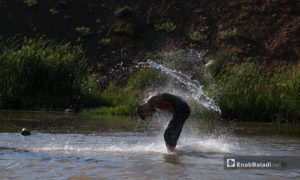 شاب يرمي على نفسه الماء في نهر حنة في عفرين - 7 آب 2020 (عنب بلدي/عاصم الملحم)