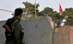 مقاتل من قسد مقابل العلم التركي في عين العرب الواقعة على الحدود السورية التركية (AFP)
