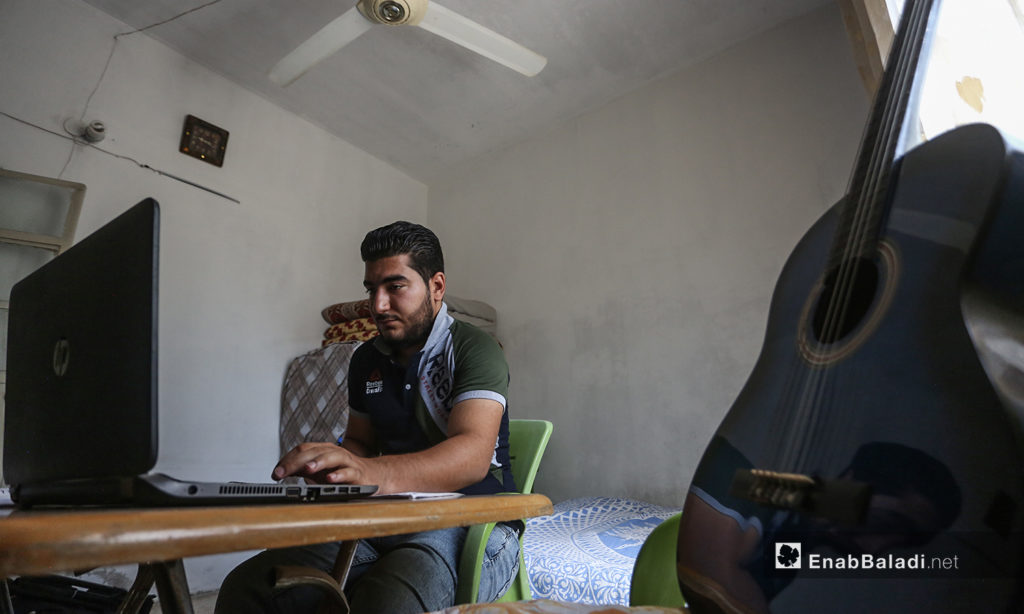 الشاب مازن الشيخ يدرس على طاولة في منزله وعلى يساره جيتار -08 أيلول 2020 (عنب بلدي/ يوسف غريبي)