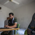 الشاب مازن الشيخ يدرس على طاولة في منزله وعلى يساره جيتار -08 أيلول 2020 (عنب بلدي/ يوسف غريبي)