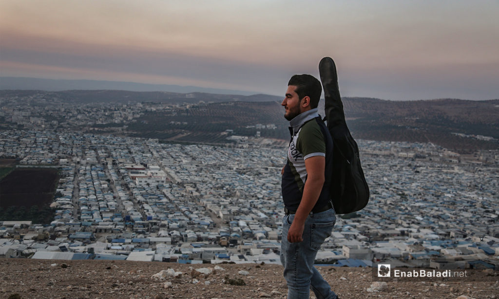 مازن الشيخ يحمل جيتاره على تله بلدة عقربات المطلة على المخيمات والقرى -08 أيلول 2020 (عنب بلدي/ يوسف غريبي)