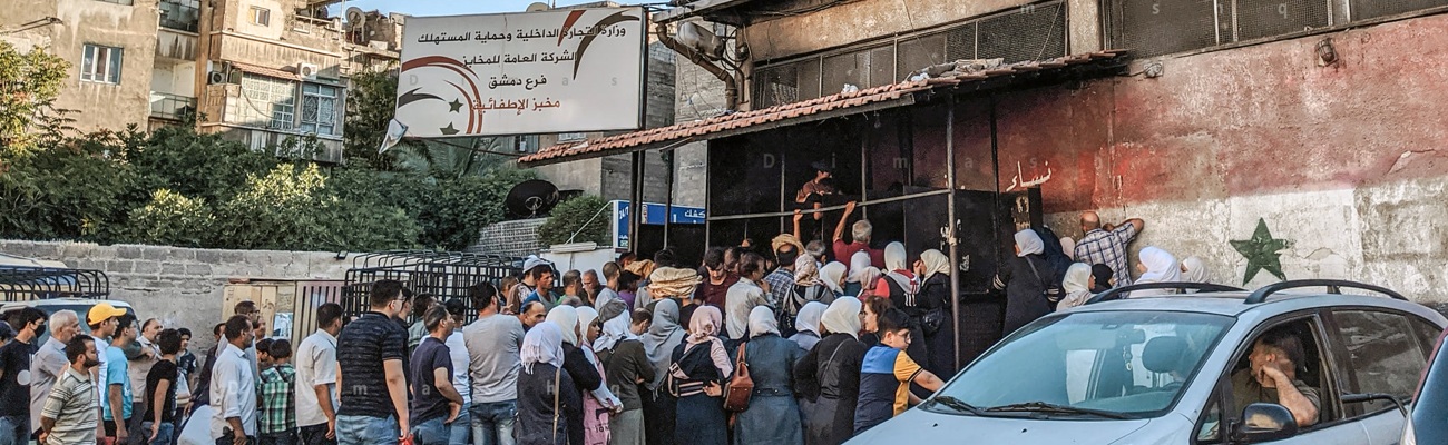 تحت لافتات حماية المستهلك طابور من المواطنين أمام باب الشركة العامة للمخابز في مدينة دمشق- 22 من تموز 2020 (عدسة شاب دمشقي)
