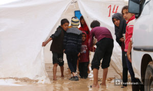 أطفال متجمعون أمام خيمة غارقة بماء المطر والوحل في مخيم 