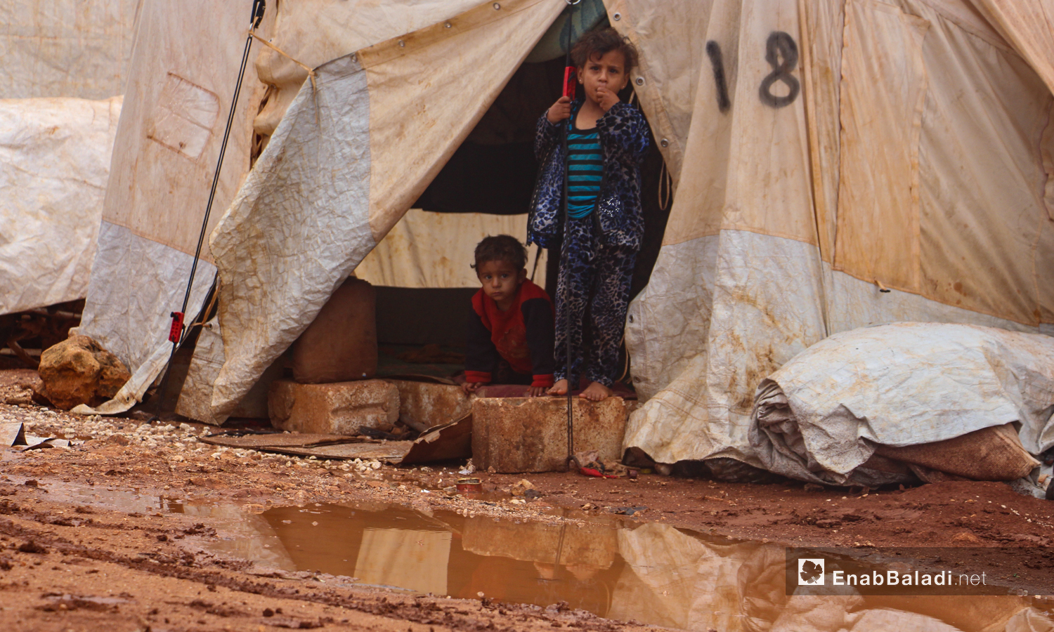أطفال يقفون على الحجارة التي تحيطها المياه بعد هطول الأمطار الغزيرة على مخيم الرمضون على أطراف قرية كفر عروق شمالي إدلب - 2 تشرين الثاني 2020 (عنب بلدي/إياد عبد الجواد)