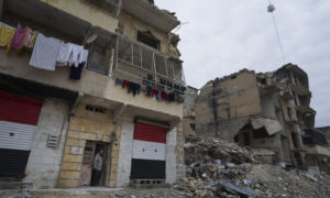 رجل يقف أمام منزله المتضرر من قصف قوات النظام على مدينة حلب والذي رسم علم النظام على واجهته بعد استعادة قواته السيطرة على المدينة - 21 كانون الثاني 2018 (AP)
