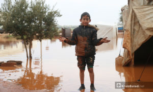 طفل يقف وسط الخيام الغارقة بمياه الأمطار في مخيم حربنوش بريف إدلب - 19 كانون الثاني 2021 (عنب بلدي - يوسف غريبي)