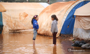 طفلتان تقفان بين الخيام الغارقة بمياه الأمطار في مخيم حربنوش بريف إدلب - 19 كانون الثاني 2021 (عنب بلدي - يوسف غريبي)
