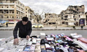بسطة لبيع الجوارب يظهر خلفها مبنى مدمر في شارع سيف الدولة في مدينة حلب - آذار 2020 (سبوتنيك)