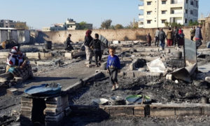 لاجئون سوريون يقفون على أنقاض مخيمهم المحترق في لبنان (الأناضول)
