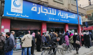 سوريون ينتظرون في طابور للحصول على مواد غذائية من أمام أحد أفرع 