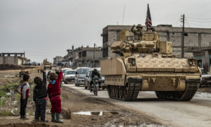 أطفال يحيون جنودًا أمريكان على ظهر عربة عسكرة في محافظة الحسكة شمالي سوريا - 17 من كانون الأول 2020 (AFP)
