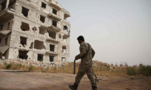 مقاتل من قوات النظام السوري يمشي أمام بناء مدمر في منطقة الراشدين بريف حلب الغربي (وكالة فرانس برس)
