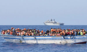 مركب مهاجرين أمام أفراد من البحرية الملكية البريطانية من سفينة هجومية من طراز ألبيون تابعة للبحرية الملكية البريطانية خلال مهمة إنقاذ في البحر الأبيض المتوسط ​​(AFP)
