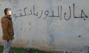 شاب ينظر إلى عبارة جاك الموت يا دكتور على حائط في درعا - 2018 (الأناضول)