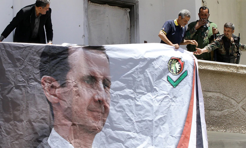 عناصر من الدفاع الوطني في سوريا يعلقون صورة رئيس النظام بشار الأسد على أحد المباني - 2015 (AFP)