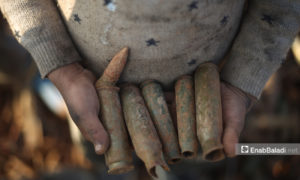 بقايا ذخيرة تالفة بيد طفل في مكب الأسلحة والذخائر بمدينة إدلب، التي يعاد جمع بعضها وبيعها من قبل مدنيين – 5 من آذار 2021 (عنب بلدي/ يوسف غريبي)
