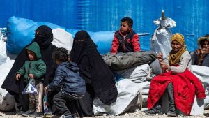  نساء وأطفال سوريون يجلسون في انتظار مغادرة مخيم الهول الذي يضم أقارب  لمقاتلي الدولة الإسلامية.
(AFP)
