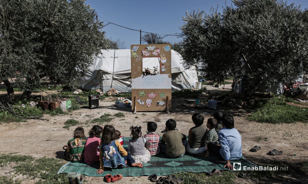 أطفال نازحين يشاهدون عرضا للدمى المتحركة قدمته فرقة الحارة المسرحية في إحدى مخيمات النازحين قرب مدينة إدلب 28 آذار 2021 (عنب بلدي/ تصوير يوسف غريبي).