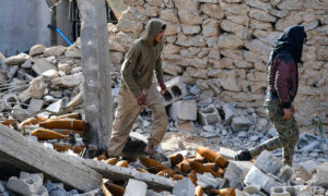 مقاتلون مع قوات سوريا الديمقراطية يمشون وسط الركام وبقايا الصواريخ في قرية الباغوز بريف دير الزور- آذار 2019 (AFP).