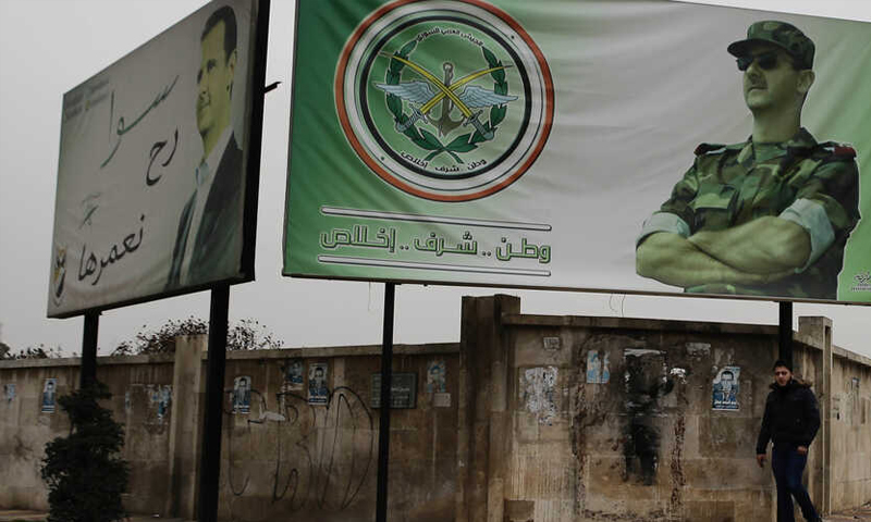 رجل يمشي وفوقه لافتة كتب عليها وطن شرف إخلاص تحمل صورة رئيس النظام السوري بشار الأسد في حلب - كانون الأول 2016 (AP)