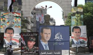 رجل يجلس بجوار تمثال للرئيس السوري السابق حافظ الأسد محاطا بملصقات انتخابية لنجله الرئيس السوري بشار الأسد في دمشق- 23 من أيار 2021 (AFP)
