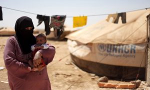 لاجئة سورية تحمل طفلًا في مخيم الزعتري في الأردن (AP)