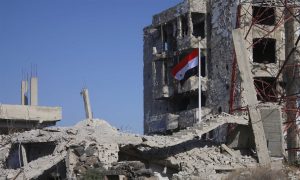 علم النظام السوري فوق حطام أبنية في مدينة درعا- 12 من تموز 2018 (AFP)