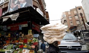 سيدة سورية تحمل الخبز على رأسها في أحد شوارع العاصمة دمشق_ 2021 (رويترز)