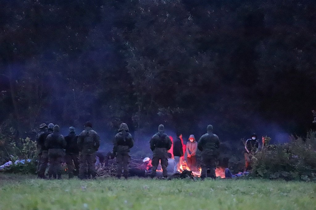 عناصر من حرس الحدود البولندي يراقبون مجموعة من المهاجرين أقاموا مخيما عشوائيا بالقرب من قرية أوسنارز جورني المحاذية للحدود مع بيلاروسيا - 18 آب 2021 (رويترز)