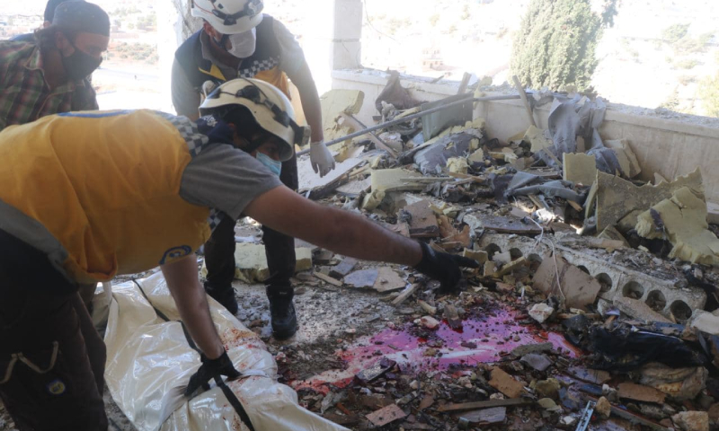 عنصران من "الدفاع المدني" ينشلان جثة قتيل بقصف لقوات النظام على سرمدا- 16 تشرين الأول 2021 (الدفاع المدني السوري)