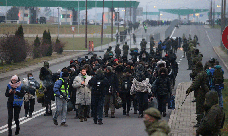 أفراد الخدمة البيلاروسية يقفون في حراسة بينما يسير المهاجرون نحو مركز النقل والخدمات اللوجستية على الحدود البيلاروسية- البولندية في منطقة غرودنو البيلاروسية – 16 من تشرين الثاني 2021 (رويترز)