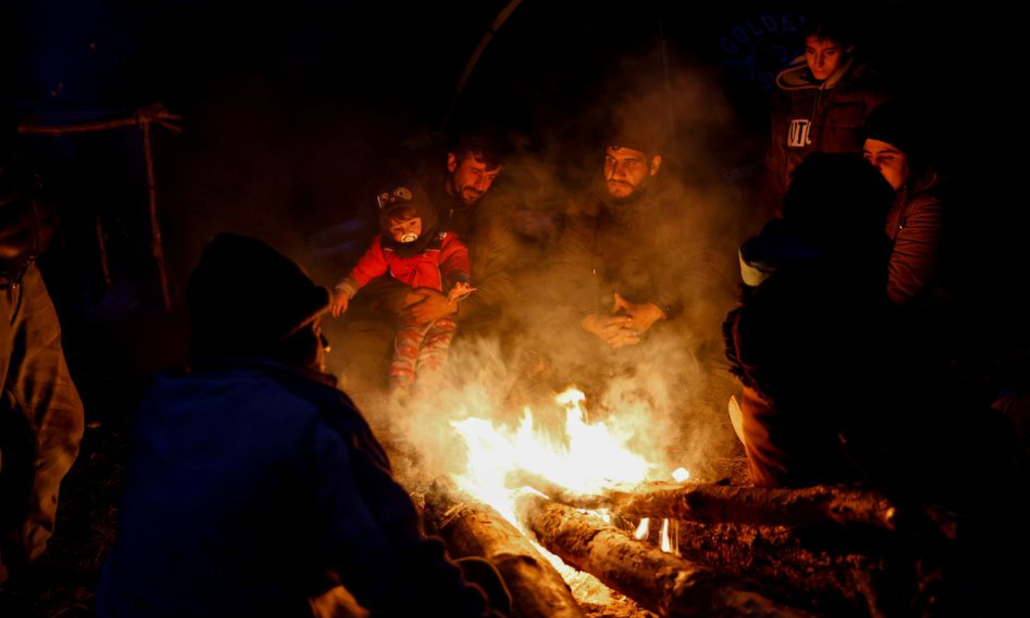 مهاجرون يتجمعون حول النار في مخيم مؤقت على الحدود البيلاروسية البولندية (رويترز)