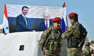 جنود سوريون يتحدثون بجانب ملصق للرئيس الروسي، فلادمير بوتين ورئيس النظام السوري، بشار الأسد عند معبر أبو الظهور في مدينة سراقب- 4 من نيسان 2018 (AFP)