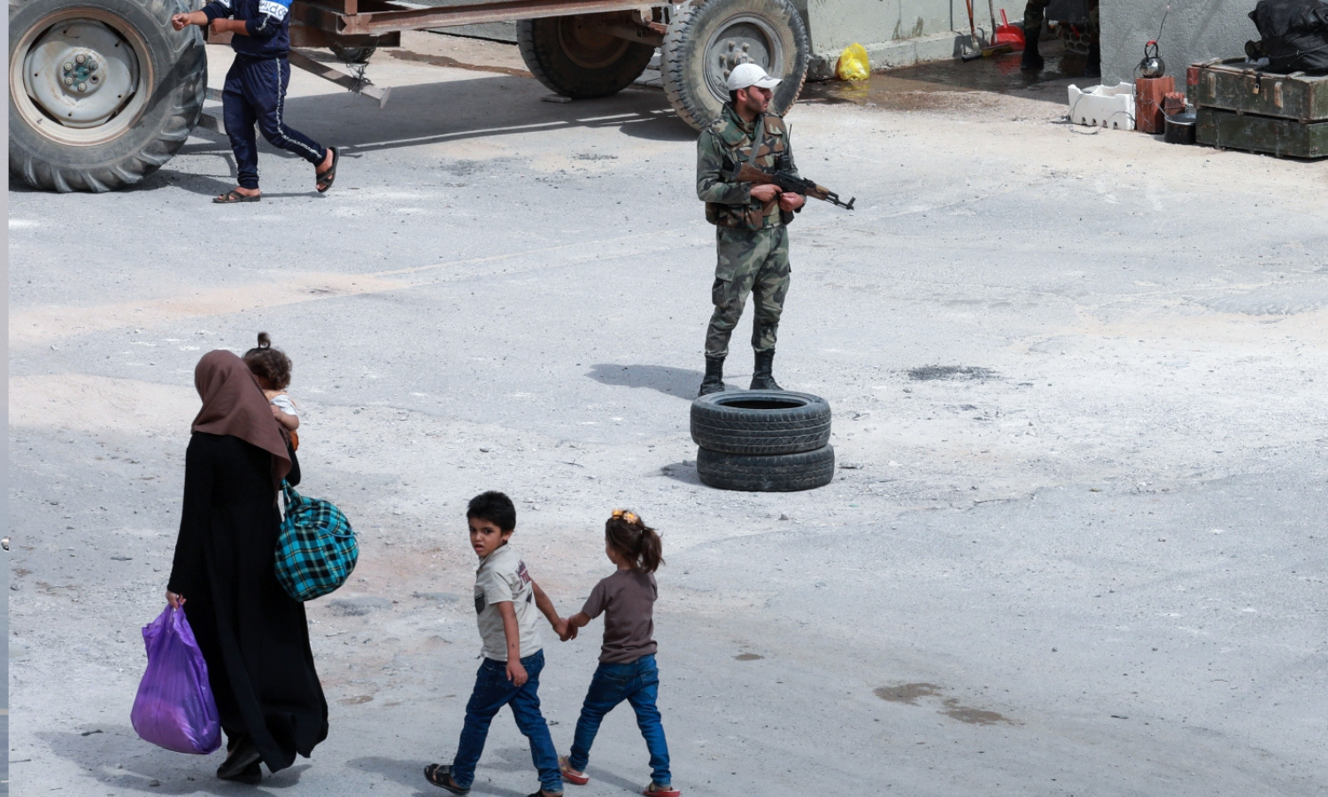 صورة التُقطت خلال جولة نظمتها وزارة الإعلام في حكومة النظام السوري، تظهر أشخاصًا يمشون أمام جنود من جيش النظام السوري عند حاجز في مديرية درعا البلد في 12 من أيلول 2021 بعد أن رفع الحصار الذي استمر شهرين ونصف الشهر- (AFP)