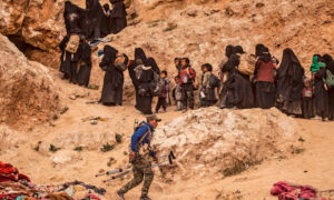 عضو في قوات سوريا الديمقراطية المدعومة من الولايات المتحدة يساعد مجموعة من الأشخاص الذين يغادرون الباغوز ، سوريا - آخر منطقة يسيطر عليها تنظيم الدولة الإسلامية - في آذار 2019 (روتيرز)

