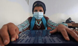 طالب سوري يعاني من إعاقة بصرية يرتدي قناعا واقيا بسبب جائحة كوفيد - 19 ويستخدم 