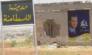 لافتة طرقية باسم مدينة اللطامنة أمام جدار مدمر لثصقت عغليه صورة كبيرة الحجم لرئيس النظام السوري بشار الأسد (شام بيرقدار/ تويتر)