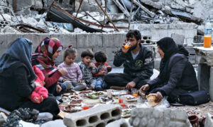عائلة تتناول وجبة الإفطار على أنقاض منزل مهدم في مدينة إدلب - 2020 (AFP)
