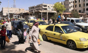 المارة أمام سيارات أجرة صفراء في مدينة درعا جنوبي سوريا- 9 من أيلول 2021 (سانا)
